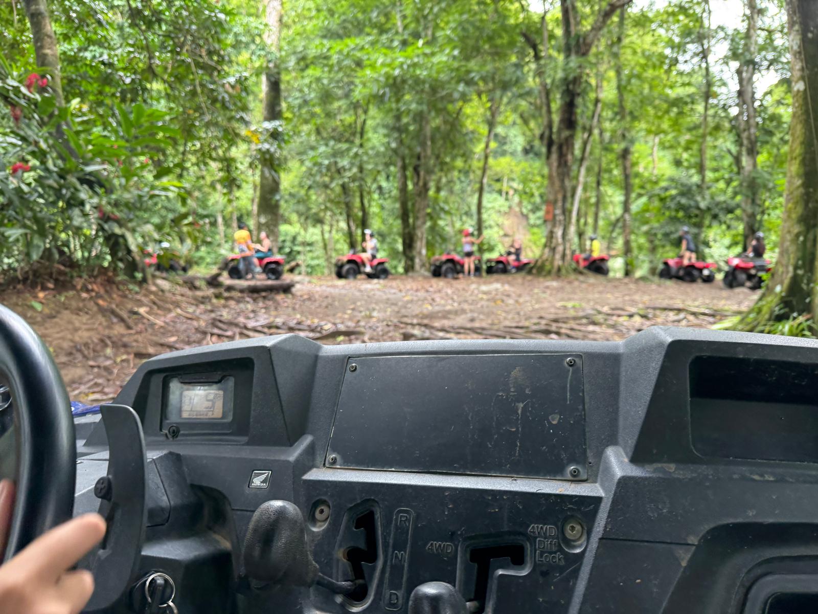 View from UTV dashboard through dense jungle with ATVs ahead